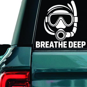 May include: White vinyl sticker featuring a scuba mask and snorkel design, with the text "BREATHE DEEP" beneath. The sticker is affixed to the rear window of a teal-coloured SUV, indicating a diving or aquatic sports theme.