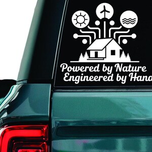 Op de afbeelding: Witte vinyl sticker met een huis, zon, windturbine en golven, met de tekst "Powered by Nature Engineered by Hand". De sticker zit op de achterruit van een teal SUV.