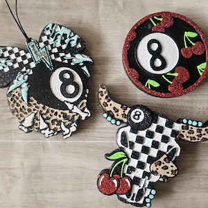 May include: Three decorative air fresheners with a black and white checkered pattern, leopard print, and the number 8. One is round with cherries, another is a skull shape, and the third is a bull skull shape.