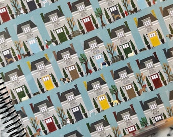 May include: A blue and white patterned planner with a repeating design of grey houses with different colored doors, trees, and dogs in front of each house.