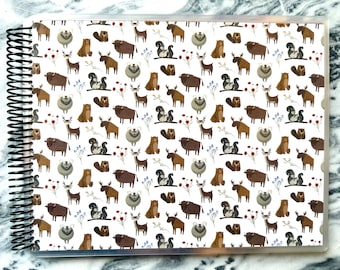 May include: A white background with a repeating pattern of brown bears, moose, deer, and squirrels. The animals are all facing forward and are surrounded by small brown branches and red and blue flowers.