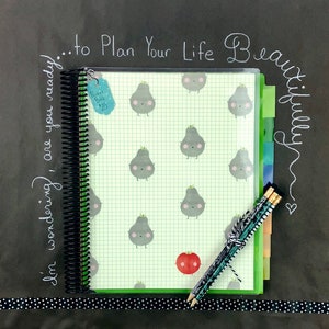 May include: A black and white spiral bound planner with a clear plastic cover. The cover has a grid pattern and a repeating pattern of cartoon pears. The planner has a green tab divider and a red tomato sticker. The text "...to Plan Your Life Beautifully" is written in white chalk on a black background.