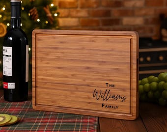 May include: A rectangular wooden cutting board with a juice groove and a handle. The board is engraved with the words "THE Williams FAMILY" in a cursive font. A bottle of red wine and a few slices of kiwi are in the background.