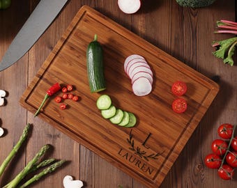 May include: A personalized bamboo cutting board with the name "Lauren" engraved on it. The board is surrounded by various vegetables, including cucumbers, radishes, and tomatoes.