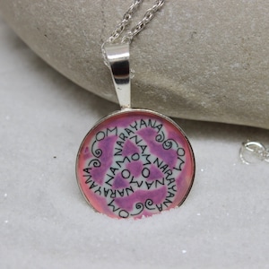 May include: A silver necklace with a round pendant featuring a pink and purple swirl design. The pendant has the word "Narayan" written around the edge in black.