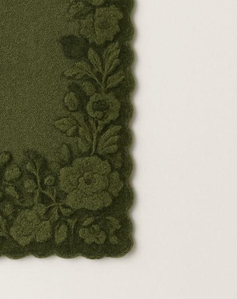 May include: A dark olive green placemat with a scalloped edge. The placemat features a detailed floral design in a raised, textured pattern. The flowers and leaves are in the same shade of green as the background.