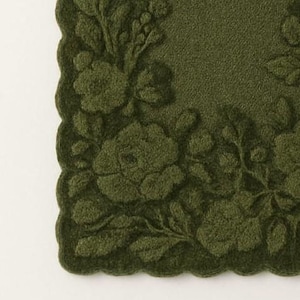 May include: A close-up of a dark green, square-shaped decorative mat with a scalloped edge. The mat features an embossed floral design, including roses and leaves. The design is a darker shade of green than the background.