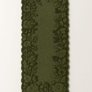 May include: Olive green rectangular rug with a floral design. The rug features a central olive green field framed by a border of embossed flowers and leaves. The edges have a scalloped trim.