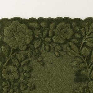 May include: A dark olive green rectangular mat with a scalloped edge. The mat features a raised floral design of roses and leaves. The background is a solid, textured green.