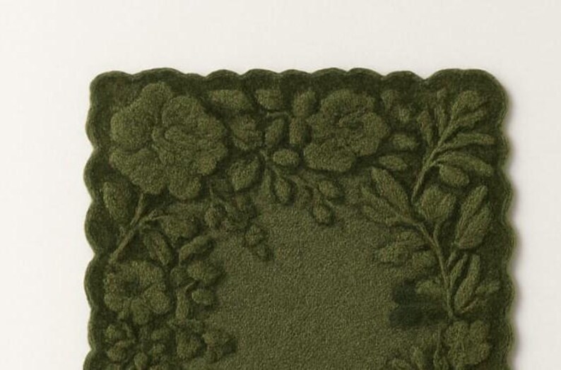 May include: A dark olive green rectangular mat with a scalloped edge. The mat features a raised floral design of roses and leaves. The background is a solid, textured green.