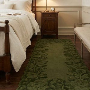 May include: A green, rectangular rug with a floral leaf design. The rug is placed in a bedroom with a wooden bed frame, a nightstand, and framed botanical prints on the wall. The rug's dimensions are approximately 36 inches wide and 72 inches long.