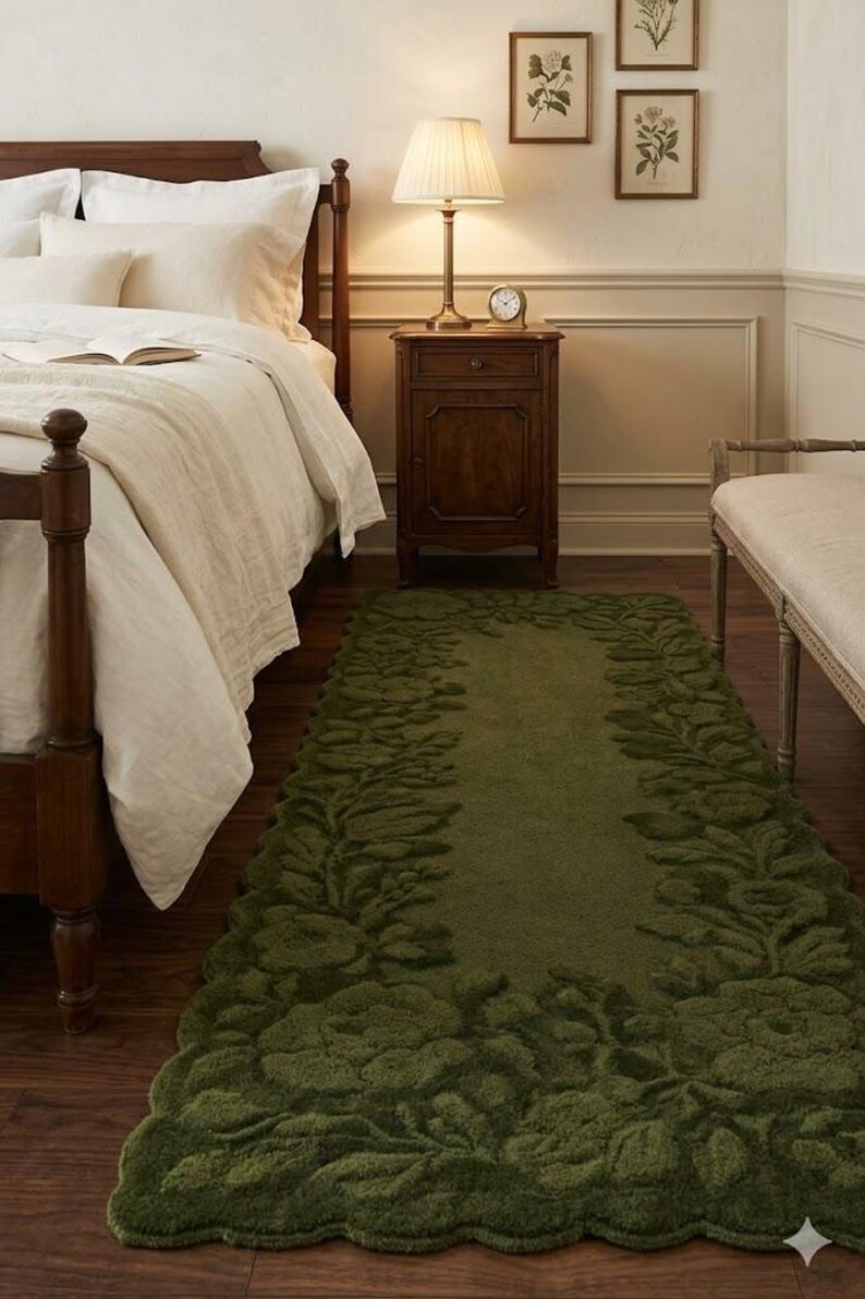 May include: A green, rectangular rug with a floral leaf design. The rug is placed in a bedroom with a wooden bed frame, a nightstand, and framed botanical prints on the wall. The rug's dimensions are approximately 36 inches wide and 72 inches long.