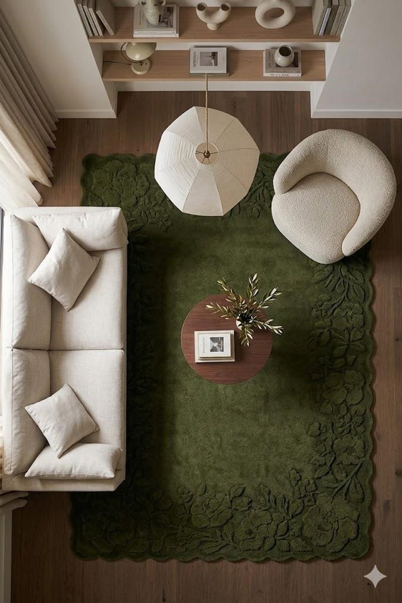 May include: Overhead view of a living room with a green floral rug, a cream-colored sofa with pillows, and a round wooden coffee table. A cream-colored armchair and a geometric pendant light are also visible.