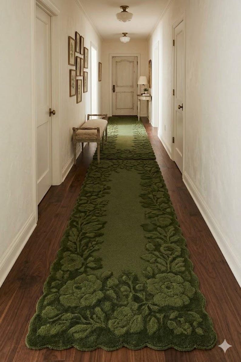 May include: A long, green floral runner rug with a scalloped edge, placed on a dark wood floor in a hallway. The rug features a raised floral design and adds a touch of elegance to the space.