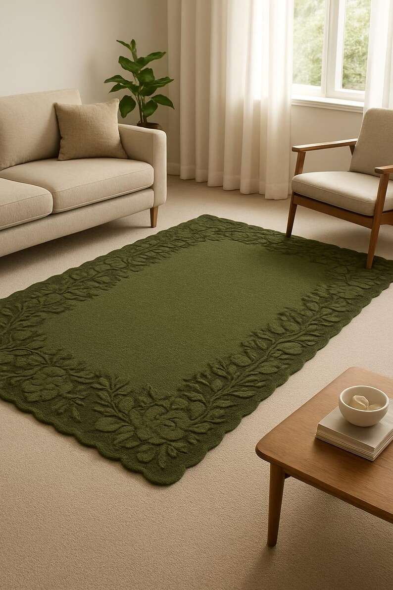 May include: A rectangular olive green rug with a floral border. The rug is placed on a light beige carpet in a living room setting. A beige sofa and armchair are visible in the background, along with a wooden coffee table.