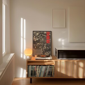K&ouml;nnte beinhalten: Ein Holzschrank mit einer Sammlung von Schallplatten, einem Plattenspieler und einem gerahmten "Berserk"-Poster. Eine kugelf&ouml;rmige Lampe und eine schwarz-wei&szlig;e Audiokomponente befinden sich auf dem Schrank. Der Raum wird von nat&uuml;rlichem Licht beleuchtet.