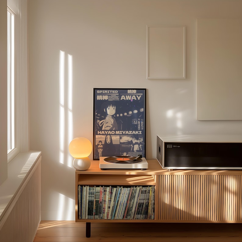 May include: A wooden record player stand with a record player, a lamp, and a framed poster of the movie "Spirited Away" by Hayao Miyazaki. The poster is in Japanese and English and features the text "Spirited Away" and "Hayao Miyazaki". The stand has shelves filled with vinyl records.