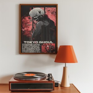 May include: A framed poster with a black and white illustration of a character from the anime Tokyo Ghoul. The poster has a red and black color scheme and the text "TOKYO GHOUL" is printed in white letters. The poster is hanging on a white wall above a record player and a lamp.