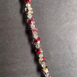 May include: A beaded bracelet with alternating clear and red square beads. The red beads have a floral design inside. The bracelet has a silver-colored clasp and chain extender.