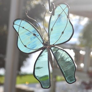 May include: A stained glass butterfly with a blue and green color scheme. The butterfly is hanging from a metal hook.