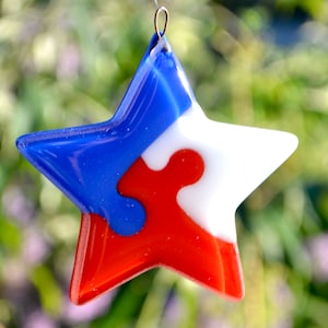 May include: A red, white, and blue glass star ornament with a silver hanger. The star is made of fused glass and has a swirling pattern.