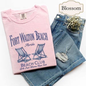 Może przedstawiać: Różowa koszulka z nadrukiem graficznym dwóch leżaków plażowych i tekstem "Fort Walton Beach, Floryda, Beach Club, Girls Just Wanna Have Sun."