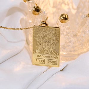 May include: A gold necklace with a pendant shaped like a trading card featuring a white dragon with the text "3000 2500" on the bottom.