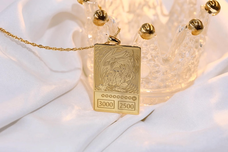 May include: A gold necklace with a pendant shaped like a trading card featuring a white dragon with the text "3000 2500" on the bottom.