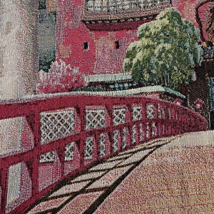 May include: A tapestry depicting a red bridge with intricate details, a green tree, and a building with a red roof. The tapestry has a textured woven fabric.