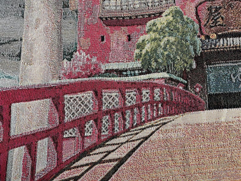 May include: A tapestry depicting a red bridge with intricate details, a green tree, and a building with a red roof. The tapestry has a textured woven fabric.