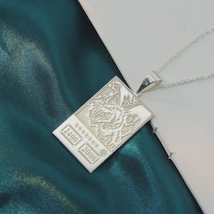 May include: A silver pendant necklace with a rectangular pendant. The pendant features a dragon design and the numbers 2400 and 2000 are engraved on it. The necklace is on a silver chain.