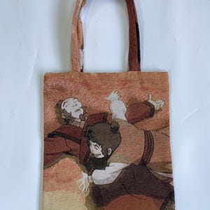 Op de afbeelding: Een tapestry tote bag met een geweven afbeelding van twee figuren in tinten bruin, rood en beige. De tas heeft bijpassende handvatten en een rechthoekige vorm. Het kunstwerk toont een scène met twee personen.