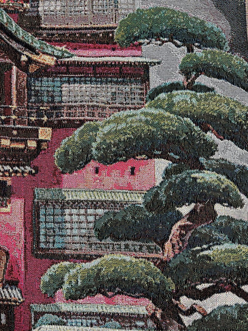 May include: A tapestry depicting a red and pink building with a green roof and several windows. The building is surrounded by vibrant green trees with brown branches.