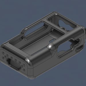 May include: A dark gray rectangular case with rounded edges and a handle on top. The case has several openings and a series of small circular holes on one side. The design appears to be a 3D model or a prototype.