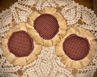 May include: Three circular fabric ornaments featuring a central dark red and cream gingham pattern surrounded by a ruffled, light tan fabric border. The items have a textured, layered appearance with visible frayed edges along the outer fabric ruffles.