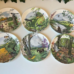 May include: Six decorative ceramic plates with nature scenes. Each plate features a different landscape with birds, animals, and plants. The plates have a white background and a detailed, colorful design.