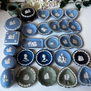 Può includere: Collezione di oggetti decorativi in ceramica blu, nera e verde. Include piatti, vassoi e portagioie con disegni in rilievo bianchi. Alcuni oggetti sono a forma di cuore o ovali, con motivi floreali e classici.