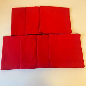 Puede incluir: Un juego de ocho servilletas de tela de color rojo brillante. Las servilletas, de forma cuadrada, están cuidadosamente dobladas, con un sutil detalle de dobladillo en los bordes. Se disponen en dos filas, mostrando su color vibrante y diseño limpio.