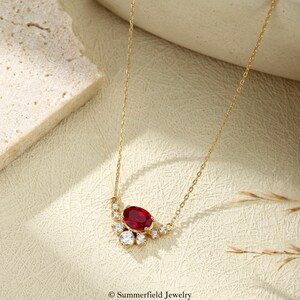 May include: A gold chain necklace featuring a central oval-cut red gemstone surrounded by a cluster of small, clear, round-cut white stones. The piece is marked with the text Summerfield Jewelry at the bottom of the frame.