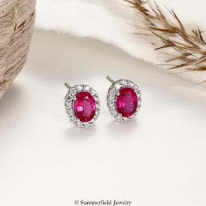 Puede incluir: Un par de pendientes de botón con piedras centrales ovaladas de color rosa vibrante rodeadas por un halo de pequeñas piedras redondas transparentes engastadas en metal plateado. El texto Summerfield Jewelry aparece en la parte inferior.
