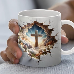 May include: White ceramic mug with a cross design. The cross is set against a backdrop of clouds and a bright sky, with a cracked effect around the image. The mug has a white handle.