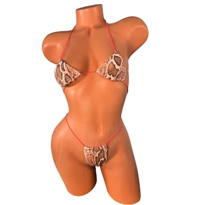Könnte beinhalten: Zweiteiliger Bikini auf einer Schaufensterpuppe. Das Bikini-Oberteil und -Unterteil haben ein Schlangenmuster in Braun- und Beigetönen. Die Träger sind leuchtend rot und bilden einen starken Kontrast. Für Bademode.