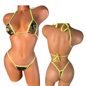 May include: A two-piece bikini set with a camouflage pattern in shades of brown, green, and tan. The edges are trimmed with neon yellow. The bikini top is a triangle style, and the bottoms are a thong style.