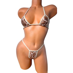 May include: A two-piece bikini set with a snakeskin pattern. The top is a triangle style with halter straps, and the bottom is a thong style. The edges of the bikini are a light cream color.