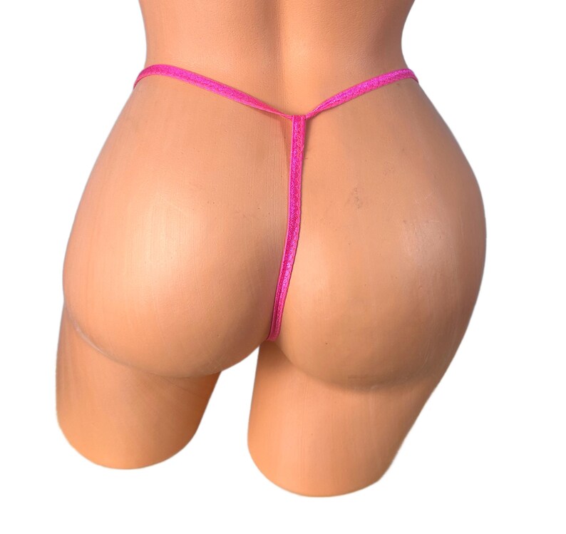 K&ouml;nnte beinhalten: Nahaufnahme eines pinkfarbenen String-Tangas. Der Tanga besteht aus einem d&uuml;nnen, zarten Material und hat ein schlichtes Design. Der Tanga wird auf einer Schaufensterpuppe pr&auml;sentiert.