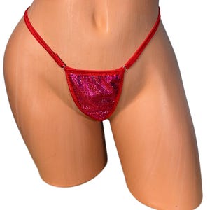 Może przedstawiać: Czerwone stringi bikini z błyszczącym, teksturowanym panelem przednim. Cienkie paski i przedni panel są w żywym czerwonym kolorze. Figi bikini są prezentowane na manekinie.