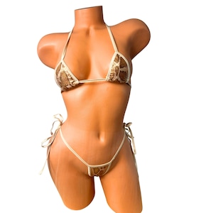 Może przedstawiać: Dwuczęściowy zestaw bikini z wzorem skóry węża. Góra to trójkątny styl z ramiączkami na szyję, a dół to styl stringów z wiązanymi bokami. Bikini jest prezentowane na manekinie.