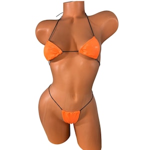 May include: Bright orange bikini set with black string ties. The triangle top and thong-style bottom are displayed on a mannequin. The bikini is made of a shiny, smooth material.