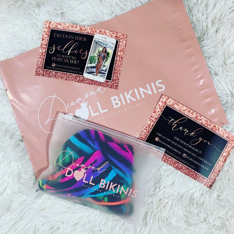 May include: A pink padded mailer with a clear plastic bag containing a colorful bikini. Two business cards and a phone with a bikini model are also visible. The text on the mailer reads "Diamond Doll Bikinis".