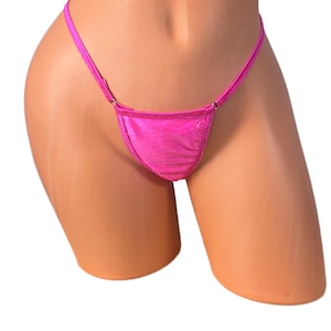 Könnte beinhalten: Ein leuchtend pinkfarbener String-Bikini-Slip. Der Stoff hat ein strukturiertes Aussehen. Der Bikini-Slip wird auf einer Schaufensterpuppe präsentiert. Die Träger sind dünn und zart.